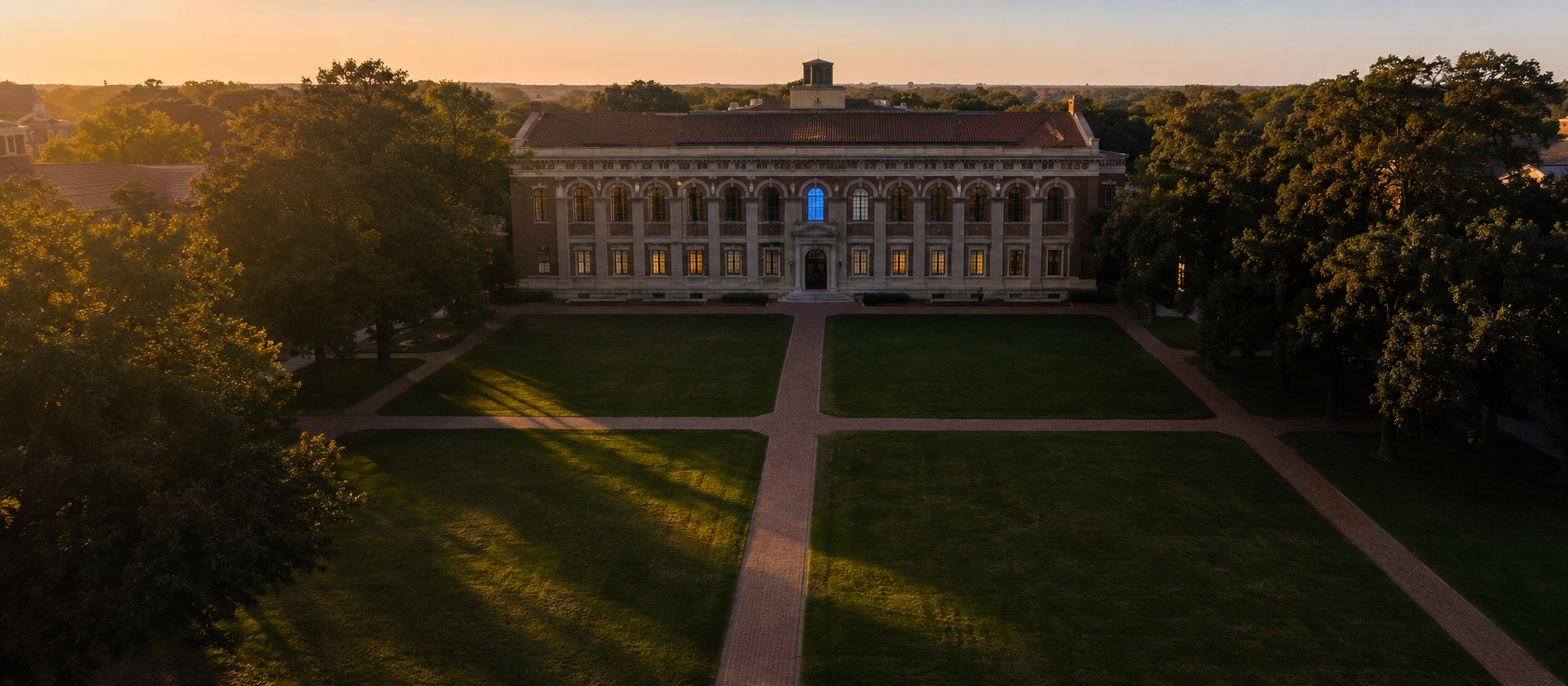 Aerial view of a classical university quad at golden hour — symmetrical brick walkways crossing a manicured lawn, a stone library at the far end with one window glowing cyan-blue.
